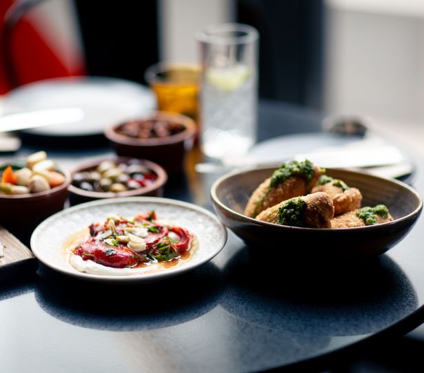 An assortment of Spanish dishes arranged on a table with a narrow depth of field, with drinks and various small sharing plates nestled between the large dishes.